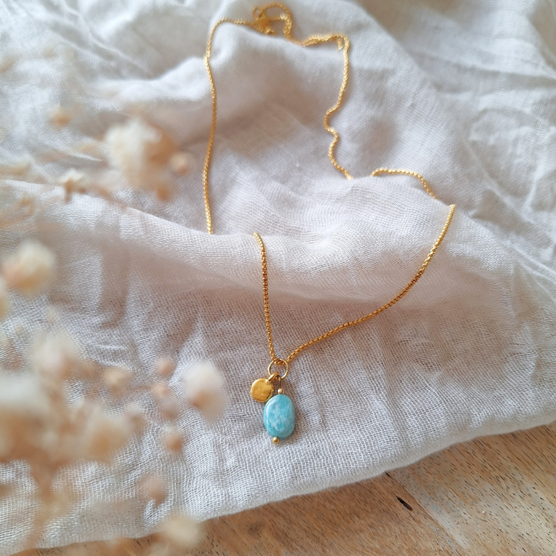 Detail van amazoniet ketting met gouden bedeltje op stof