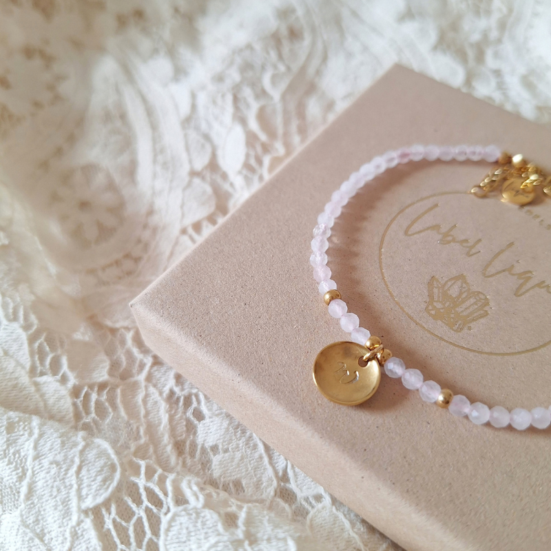 Armband met rozenkwarts en letter op een doosje, liggend op kanten stof