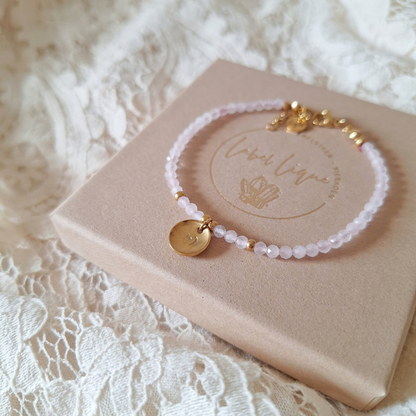 Handgemaakte rozenkwarts armband met letter op sieradendoosje en kanten achtergrond