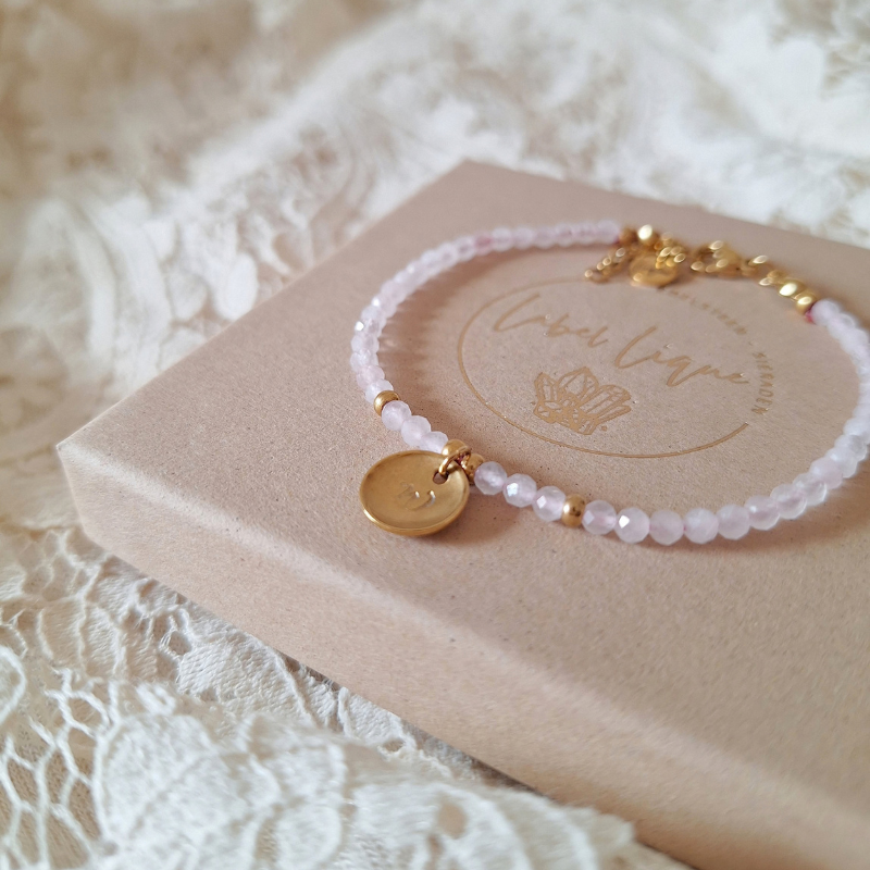 Rozenkwarts armband met letter op een sieradendoosje met kant als ondergrond