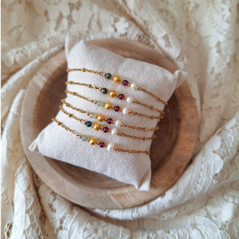 Handgemaakte armband Geloof in Jezelf met zoetwaterparel, granaat en toermalijn op een linnen kussentje in een houten bakje.